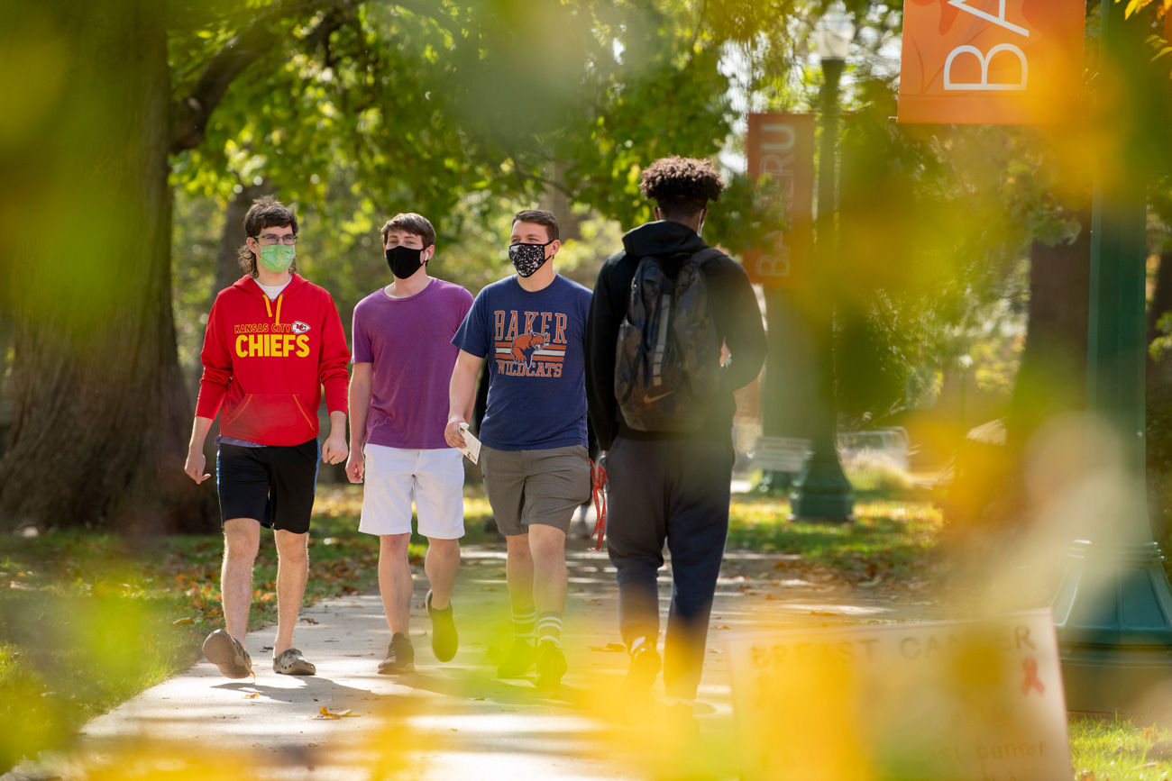 Three male students are walking across campus in early fall 2020 wearing masks.