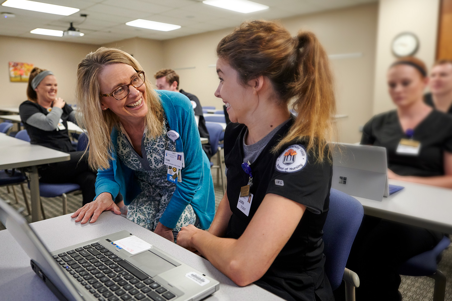 Nursing faculty and an undergraduate nursing students in discussion in a classroom.