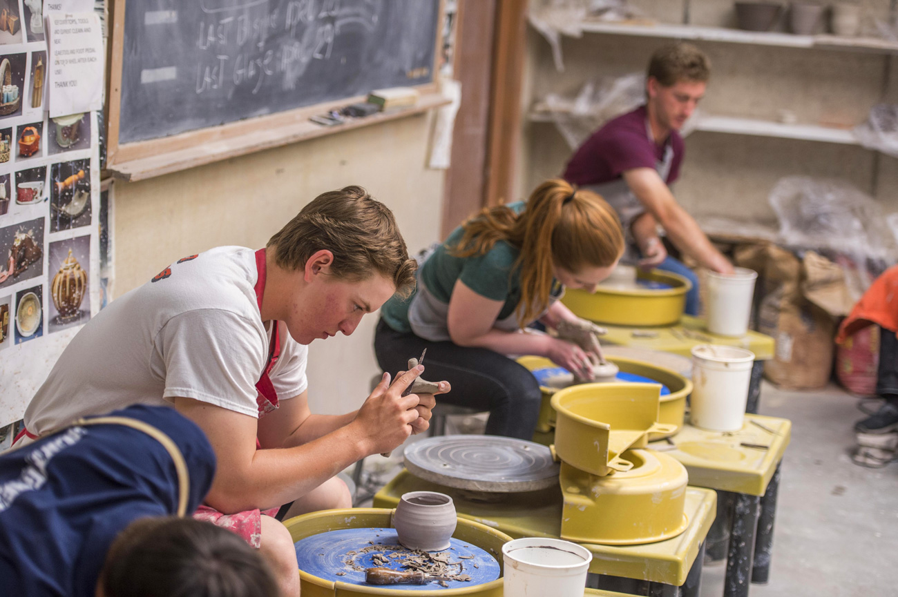 Four students throwing clay in ceramics class