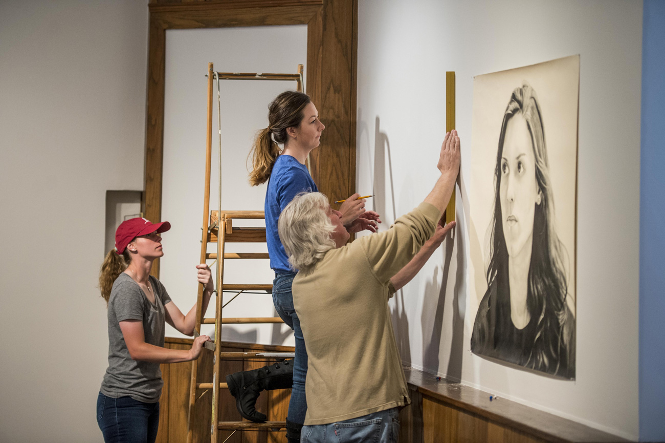 Professor Russ Horton with two female students hanging art work