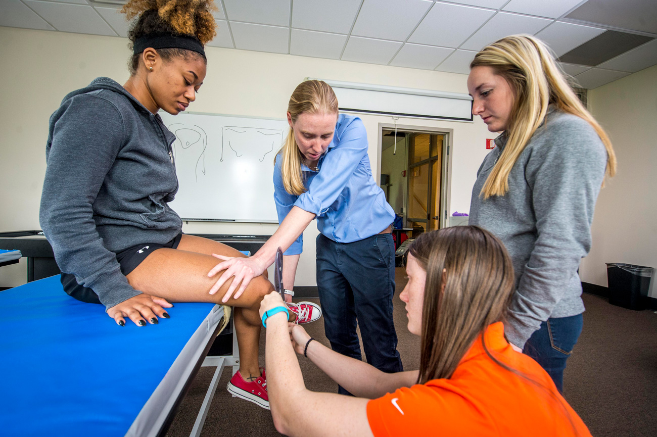 Female exercise science students and Professor examining classmate for activity