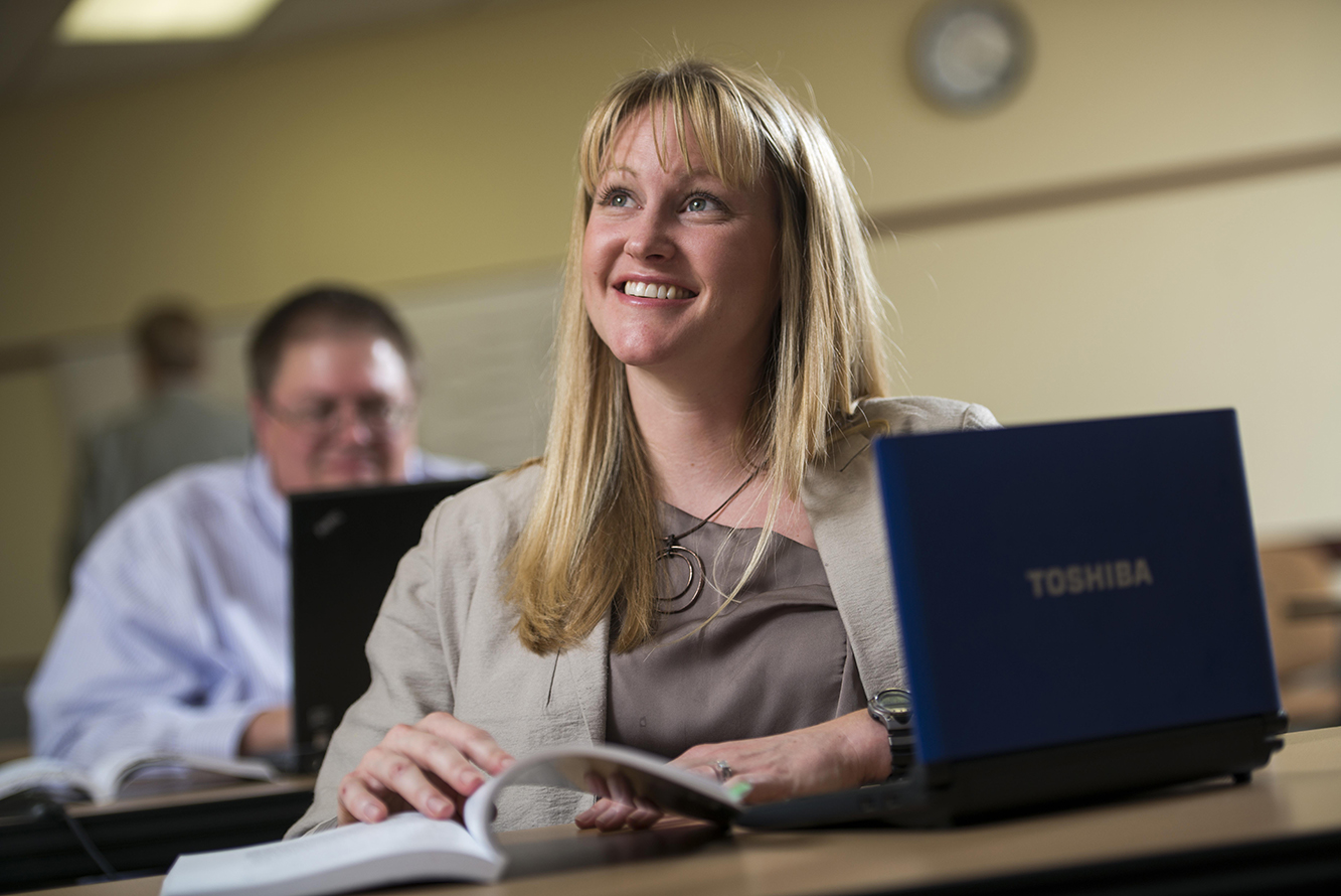 a masters instructional design & performance technology student siting at desk with a textbook and laptop