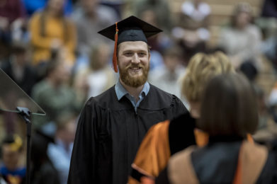 Graduating student in a cap and gown smiling at commencement