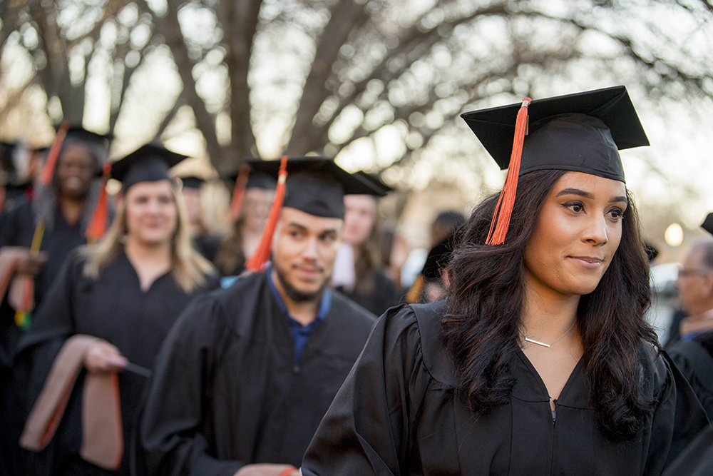 Graduating students with caps and gowns walking on campus in a line