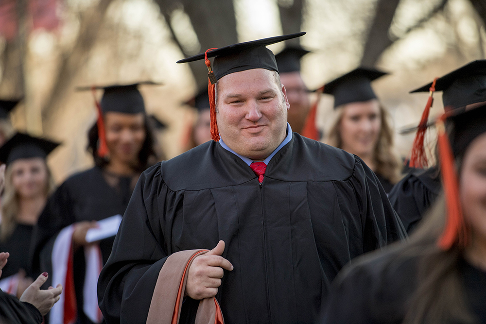 Graduating students with caps and gowns walking on campus in a line