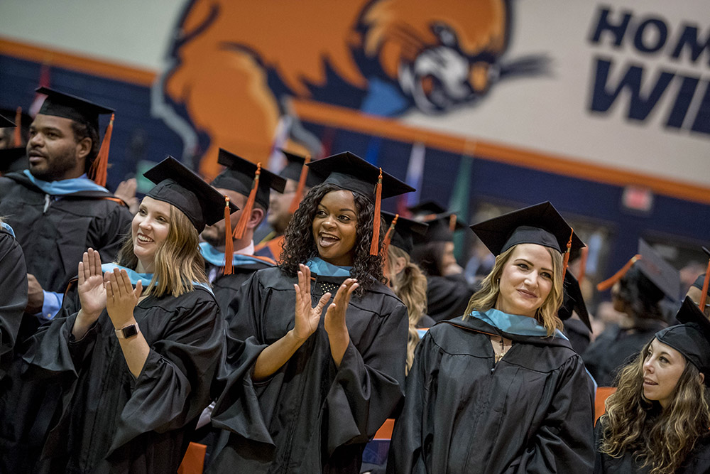 Master's program students in their caps and gowns clapping and celebrating during graduation ceremony
