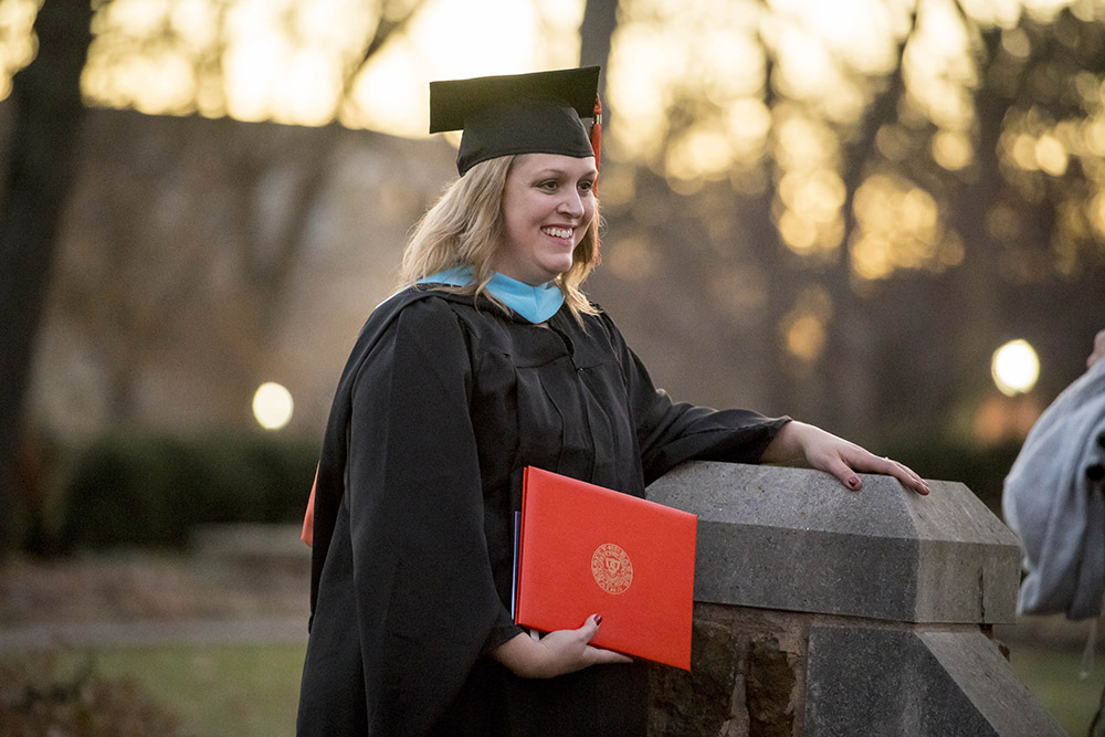 Graduating student holding diploma in a cap and gown posing for a photo