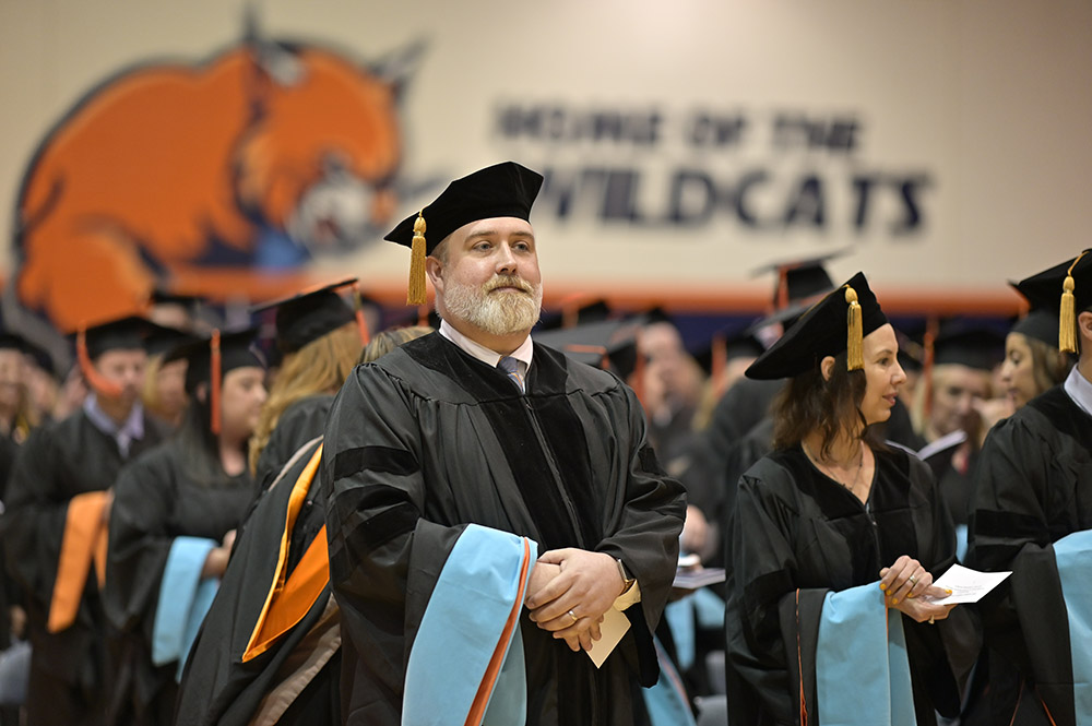 Doctoral students standing at graduation in their regalia, looking proud