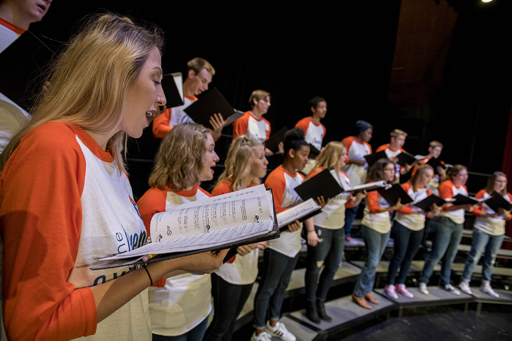 Students holding music books while singing in a choir on stage