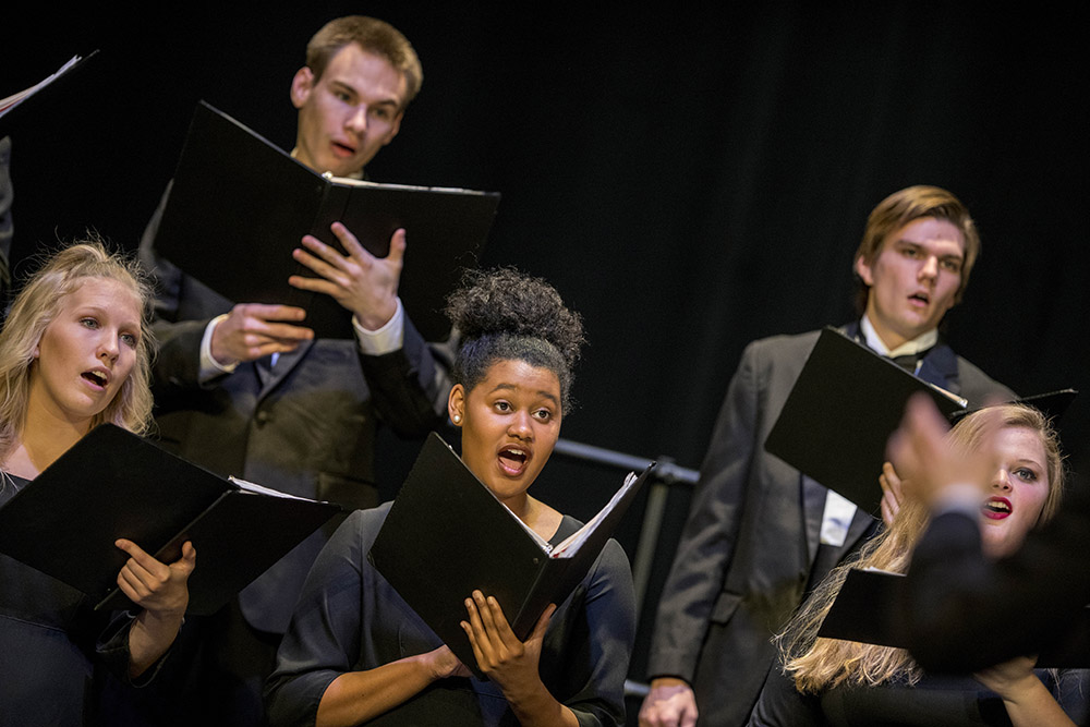 Students holding music books while singing in a choir on stage