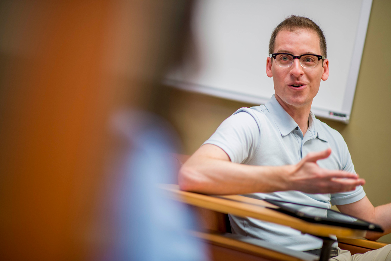 Male student sitting at a desk having a discussion with classmates