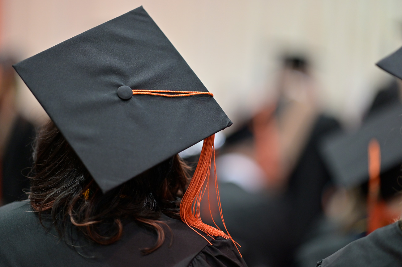 Photo of the back of a students head at commencement wearing a cap and gown
