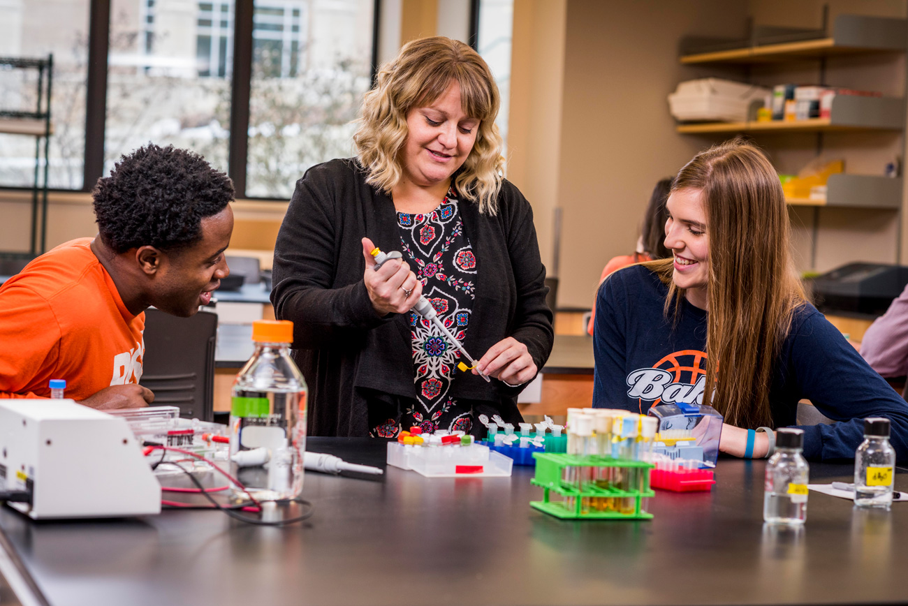 Dr. Erin Morris demonstrating an experiment to two students in a laboratory