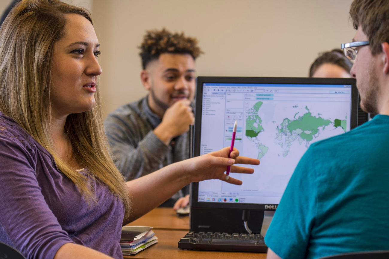 Business analytics students looking at a map on the computer and discussing a class project