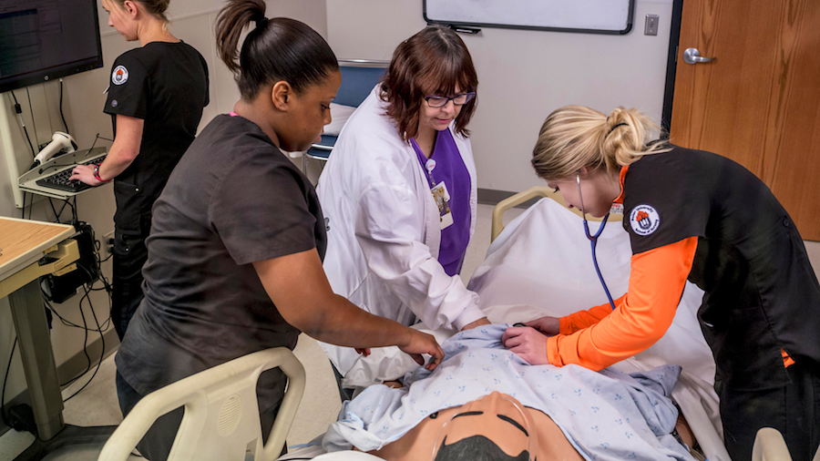 Female nursing students practicing on medical mannequin in simulation lab