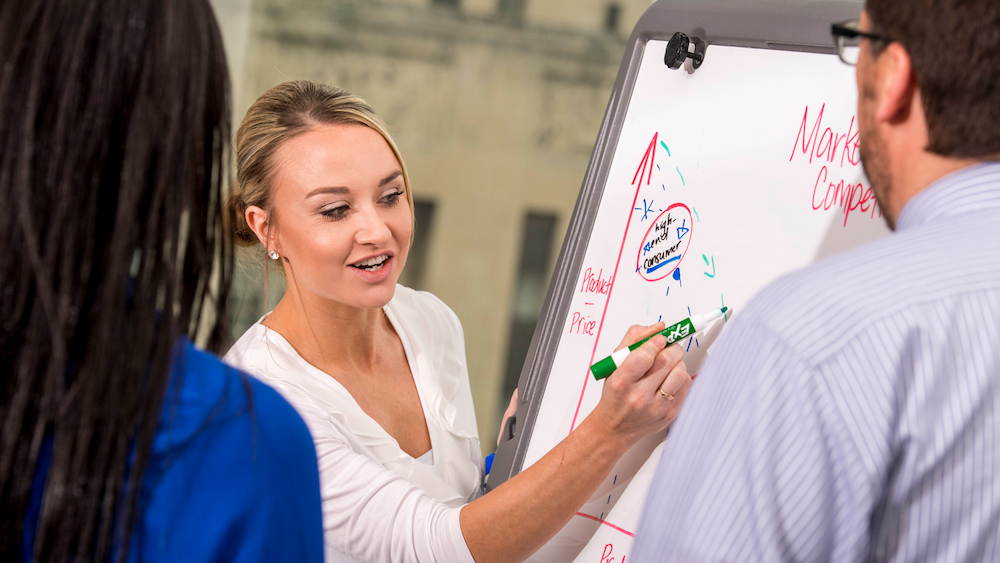 Femal business student talking with classmates while drawing a graph on a whiteboard