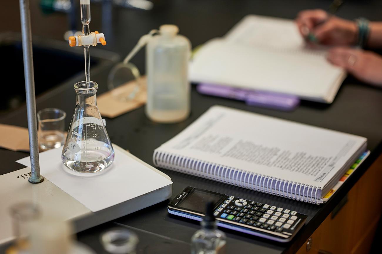 Work space of students in lab with a beaker, notes, and calculator