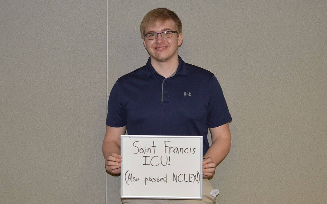 Corey True holding a whiteboard that says "Saint Francis ICU! (also passed NCLEX)"