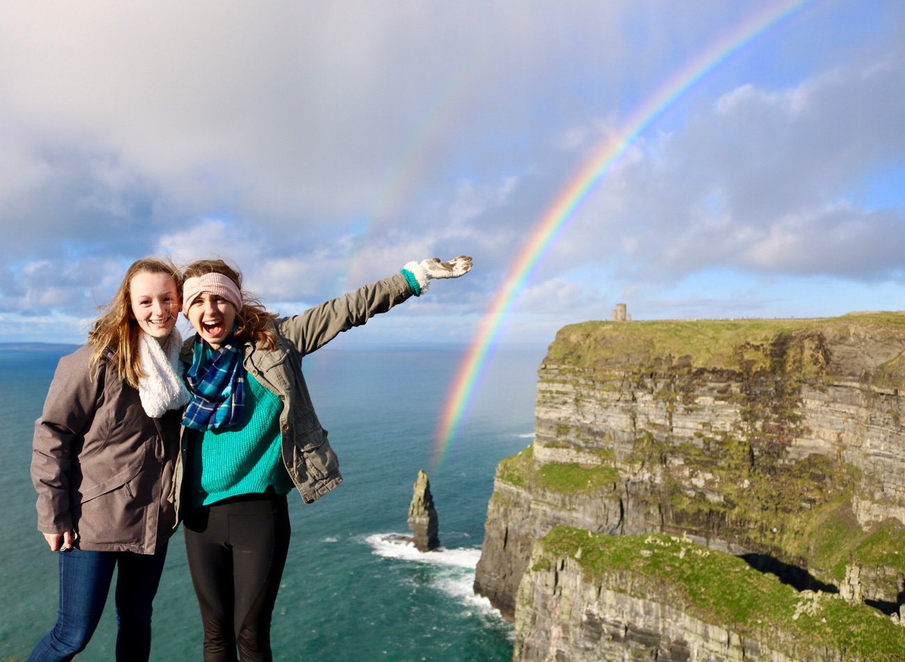 Study abroad students smiling and taking a photo with a double rainbow behind them in Ireland