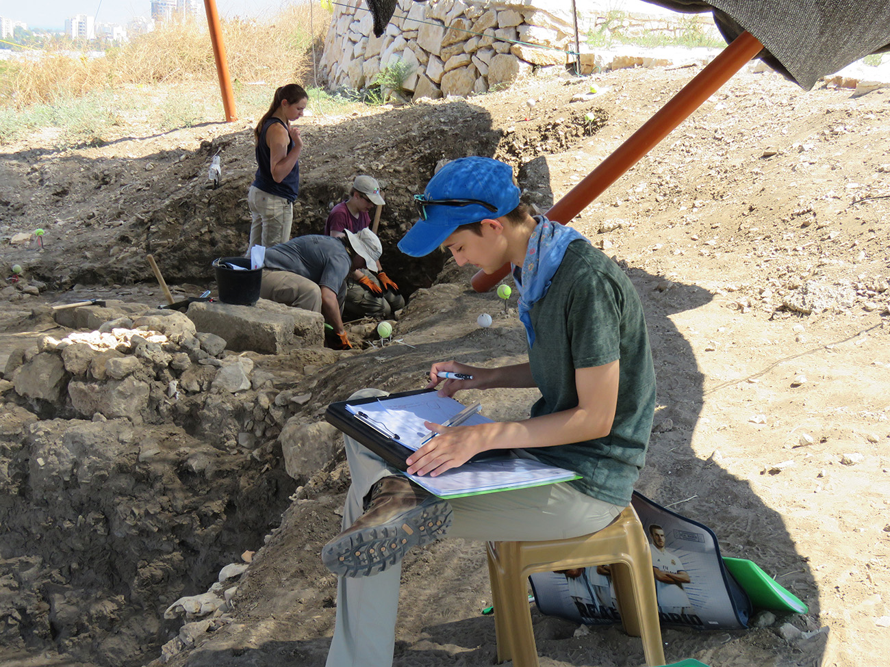 Religious Studies student sitting down and writing in a book during a excavation dig in Israel