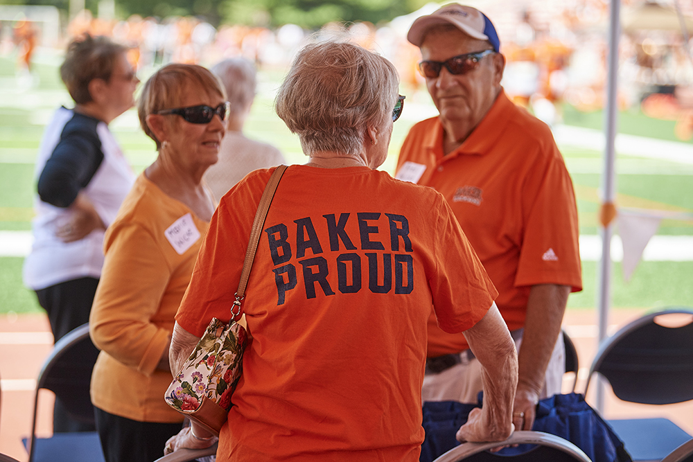 alumni in baker orange shirts at a football game, one shirt says Baker proud