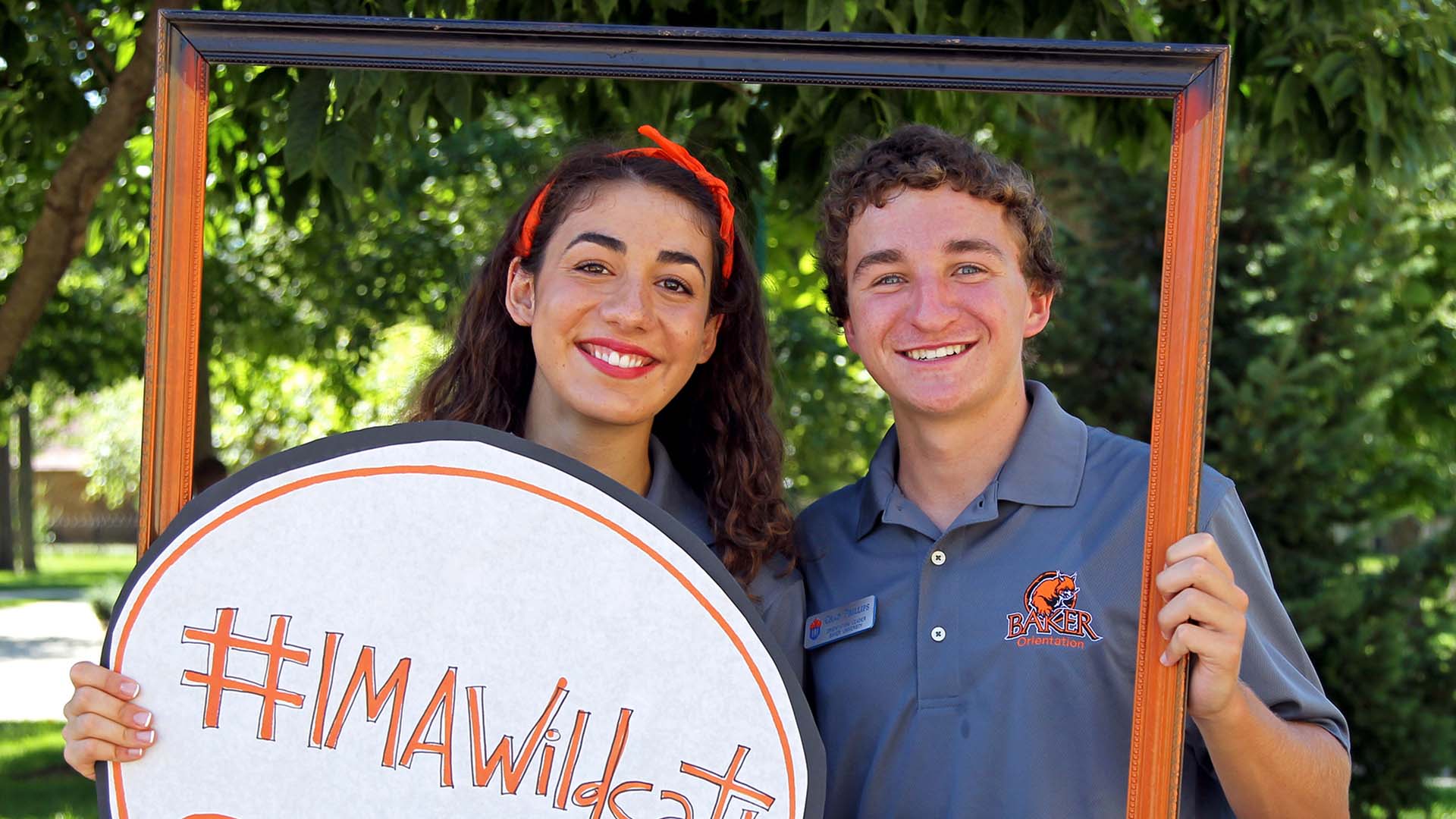 Two students smiling during orientation holding a picture frame and a sign that says Im a wildcat