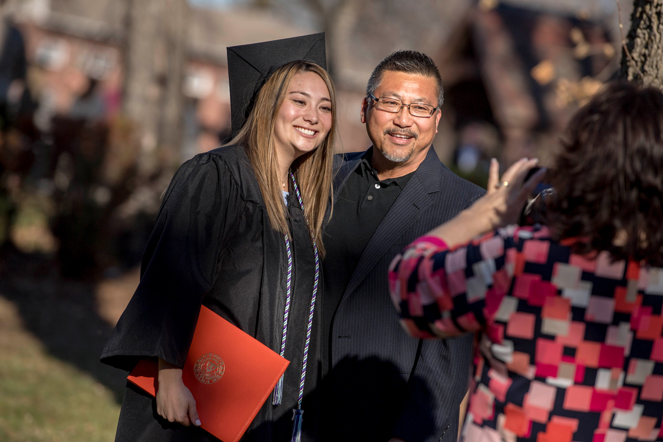 Graduate in a cap and gown smiling for a photo with her dad