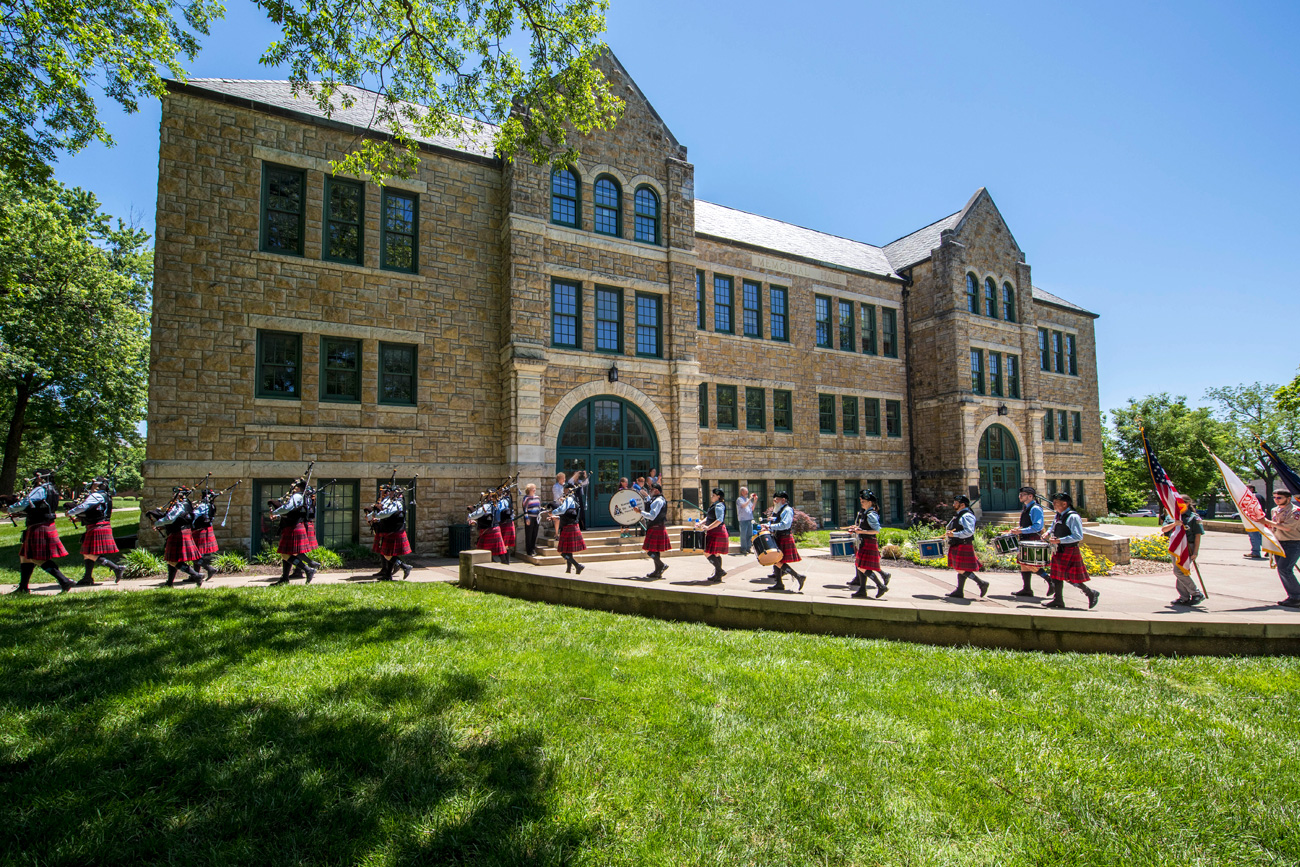 Bagpipe and drum line players walking by Mabee Hall for commencement