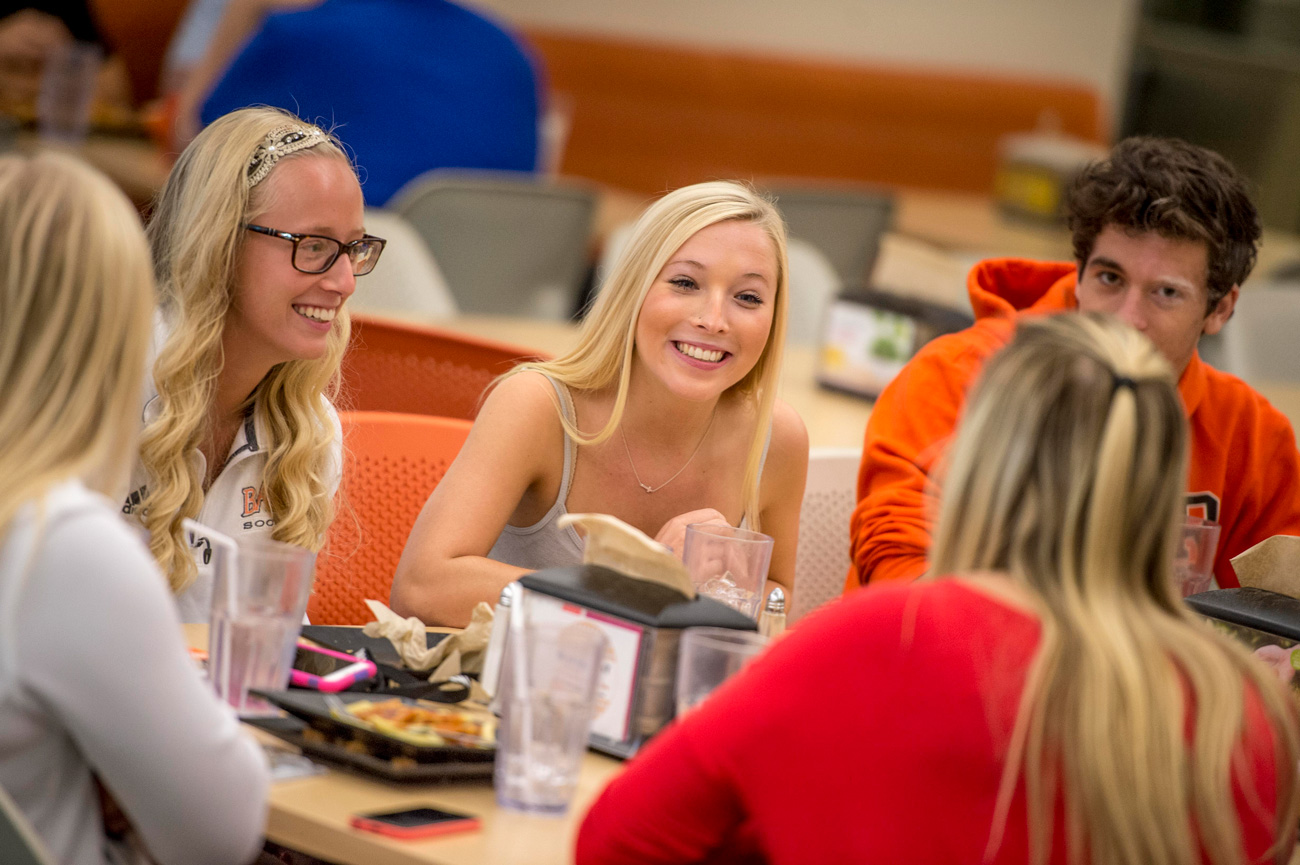 Group of students smiling at a table in the dining hall eating lunch together