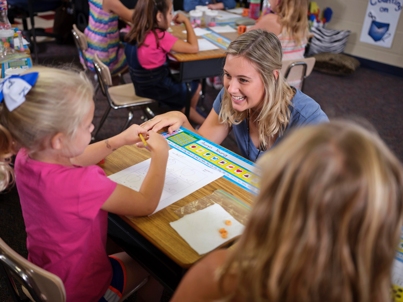 Teacher crouching down at students desk while young student is completing a worksheet