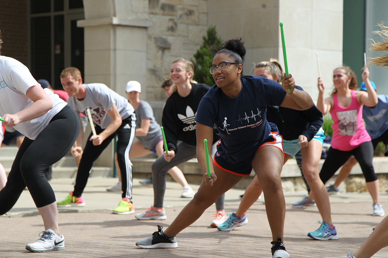 Exercise science students enjoying an exercise class outside with drumsticks in their hands