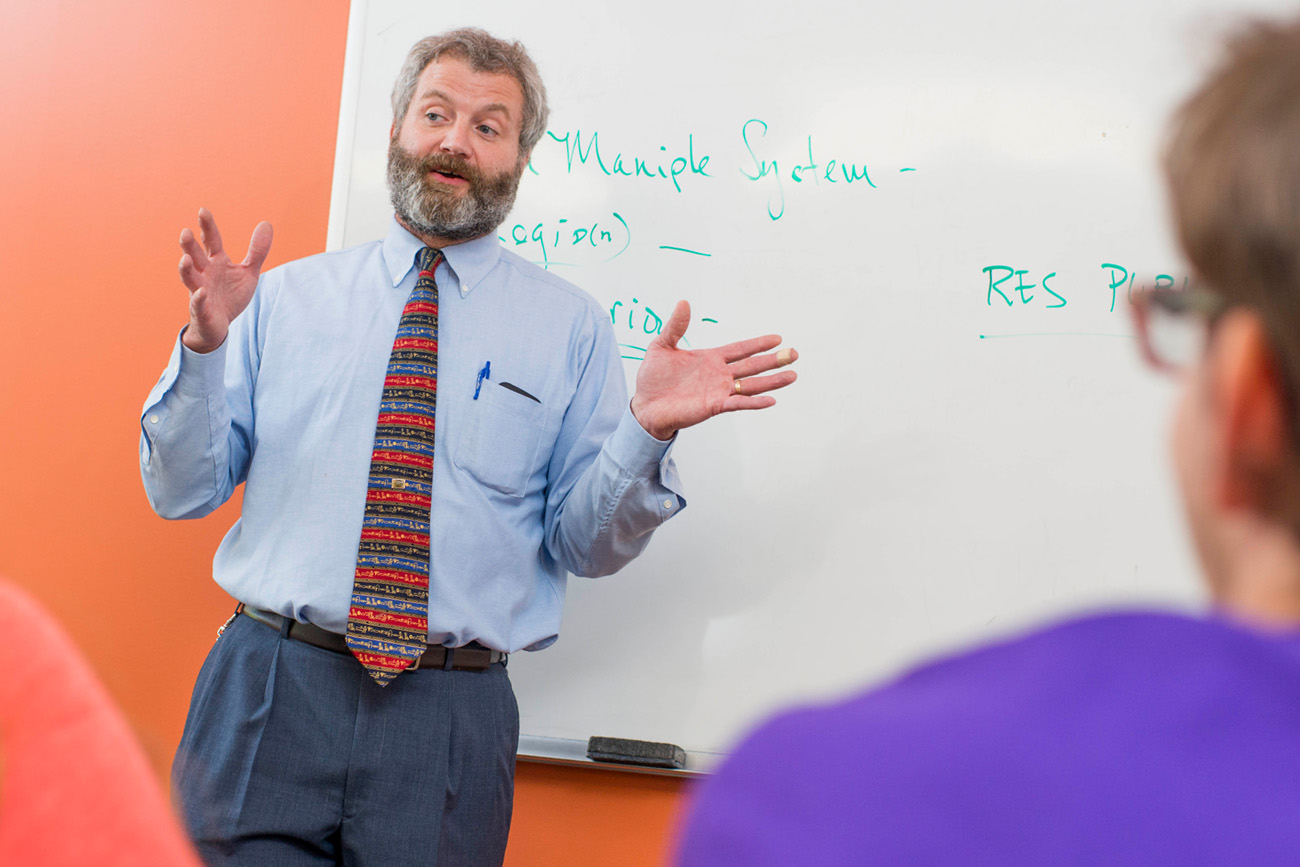Professor John Richards teaching history inside with words on the whiteboard behind him