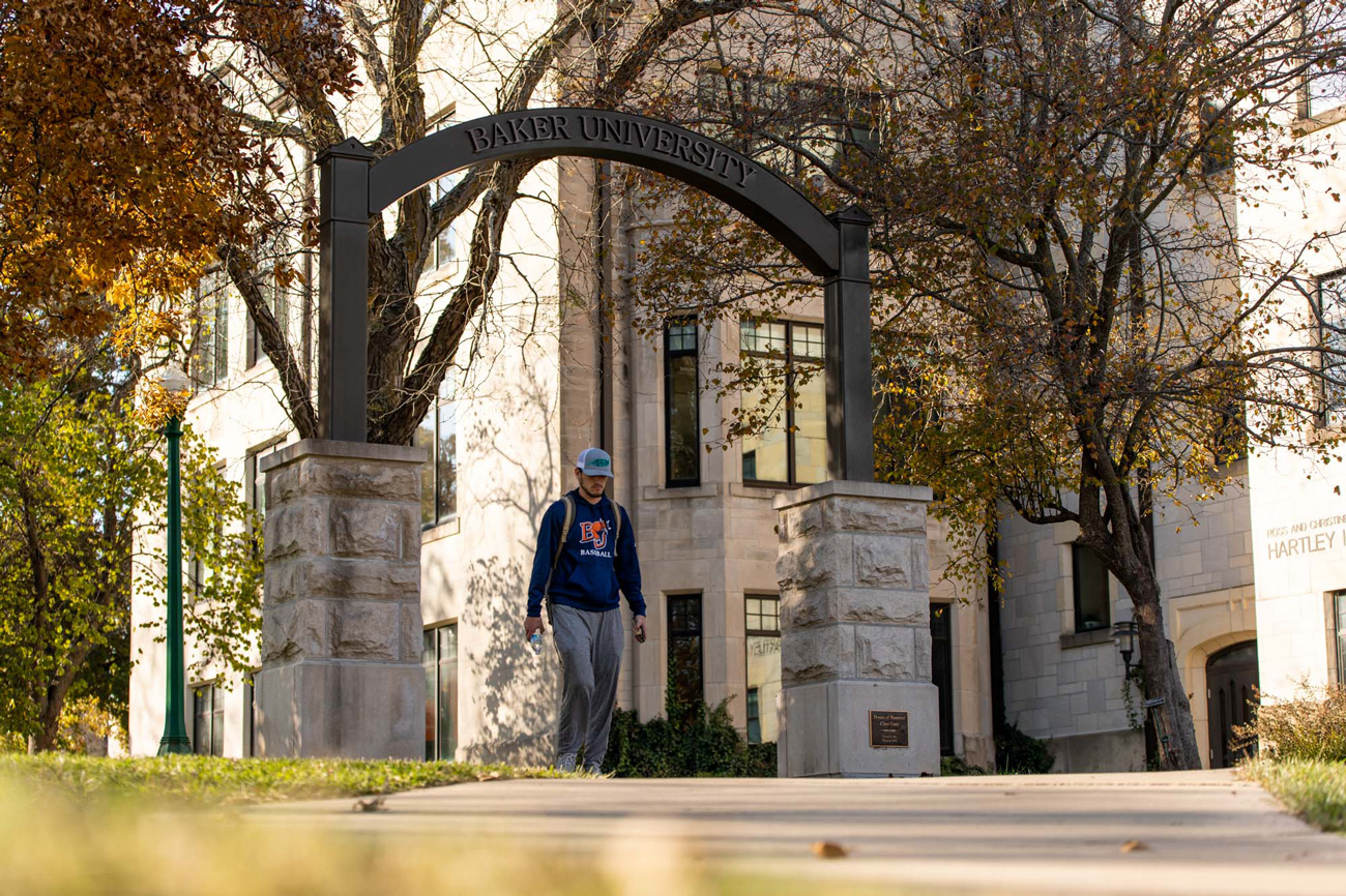 Male student walking under an iron arch that says Baker University