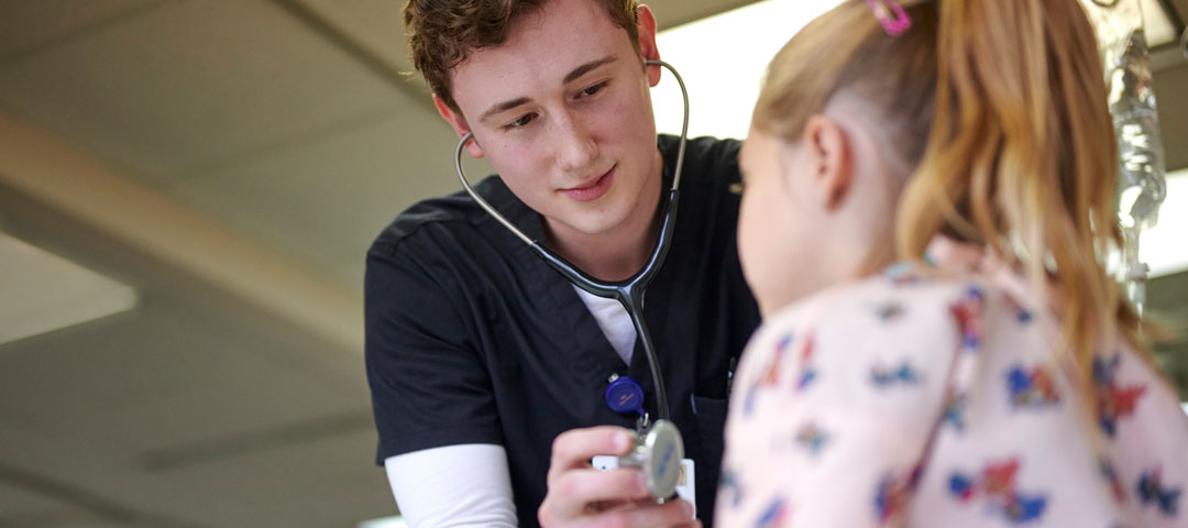 Nursing student holding a stethoscope to a young child