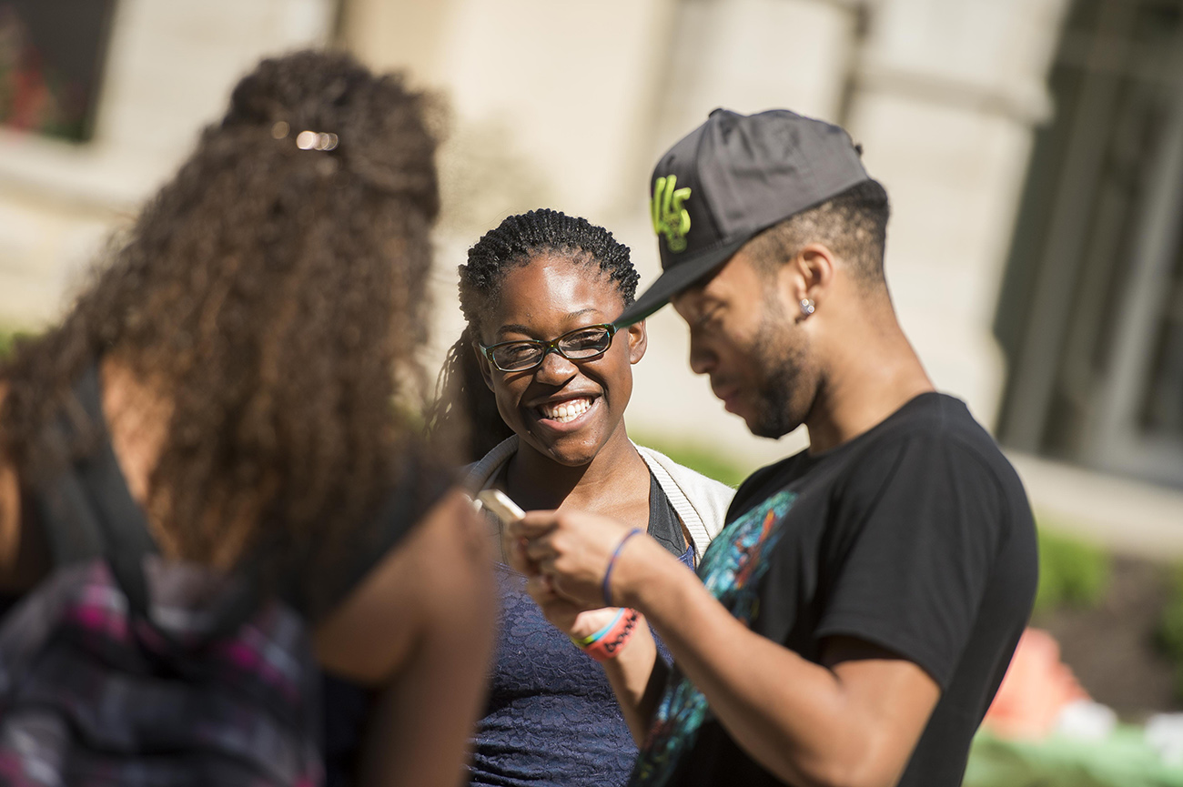 three students outside enjoying time together, looking at a phone