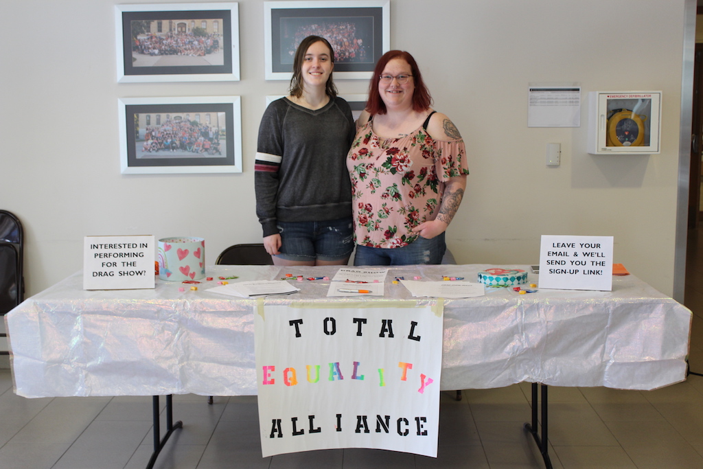 Two people standing behind a table and smiling at the camera at a Total Equality Alliance event