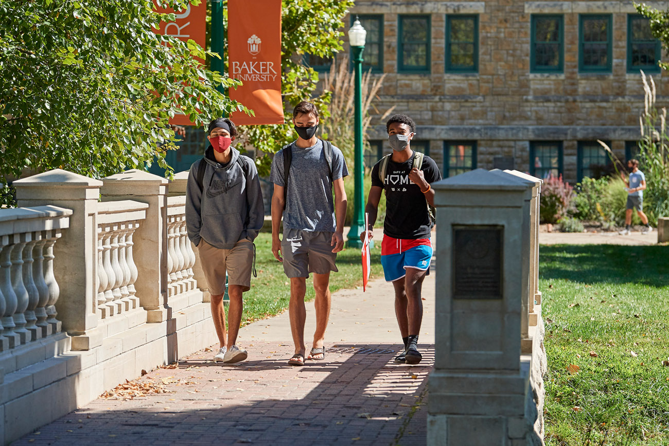 Three male students walking across Taft Bridge in the fall with masks on.