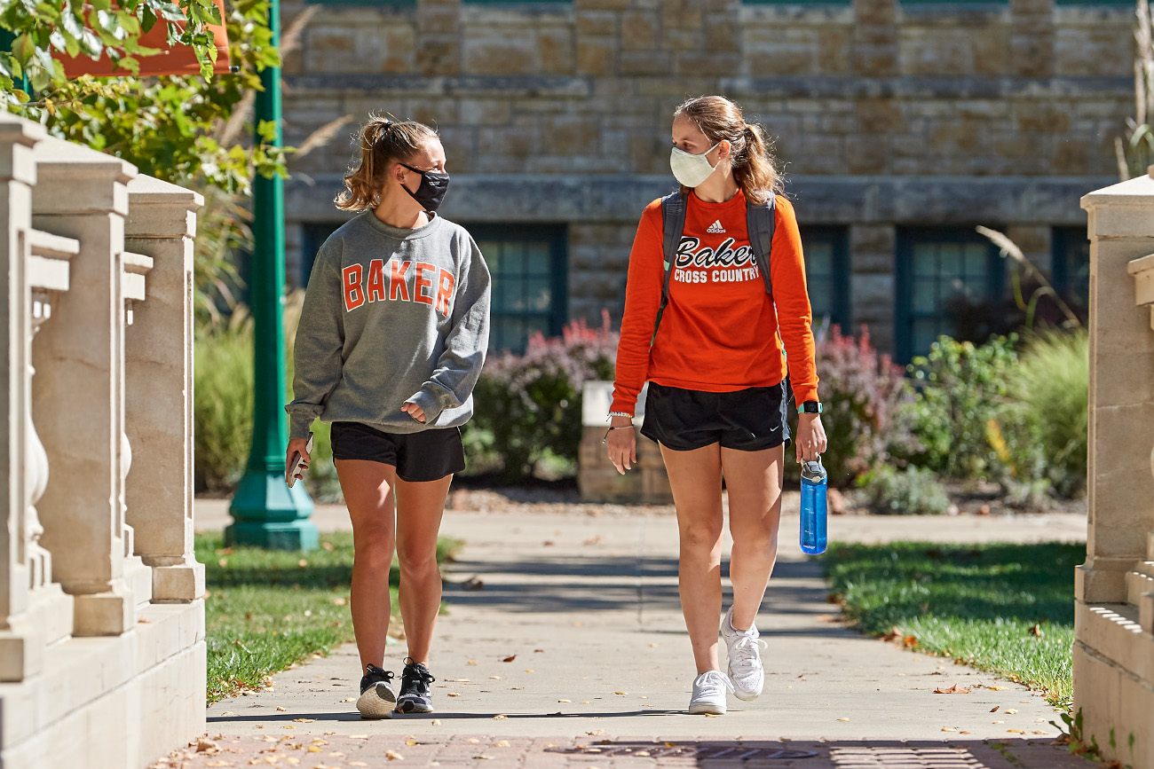 Two female students walking across campus wearing masks