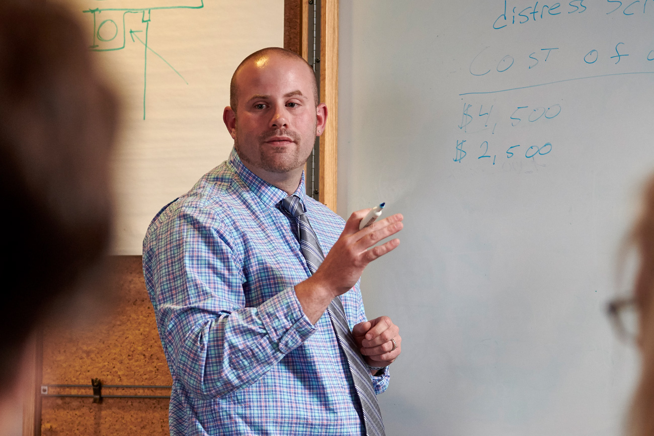 Professor demonstrating number values on a whiteboard to a class