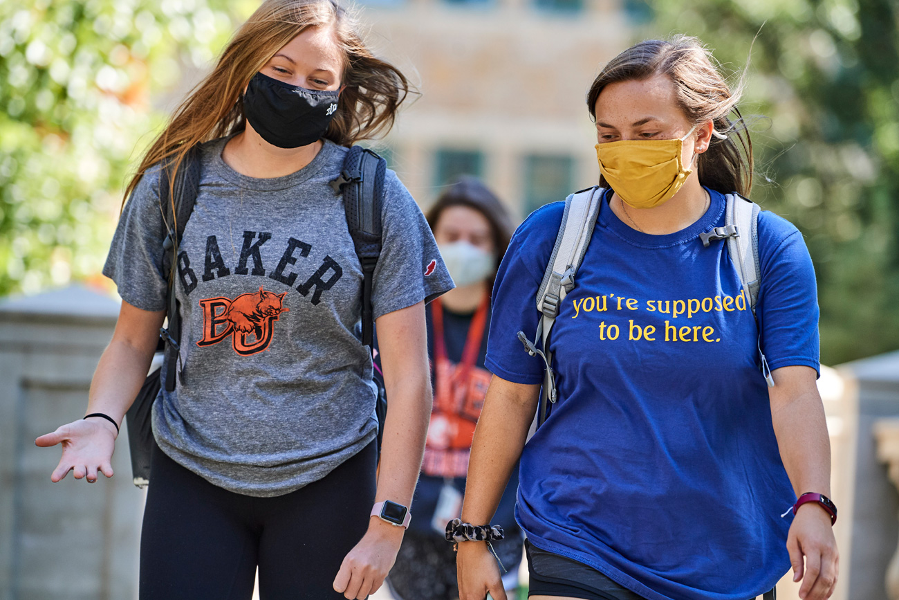 Two female students are walking across campus in early fall 2020 wearing masks.
