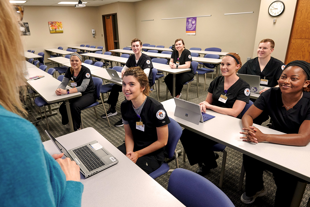 Seven nursing students listening to their professor in a classroom