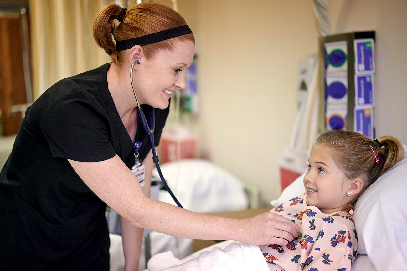 Female nursing student checking heartbeat of a little girl with a stethoscope