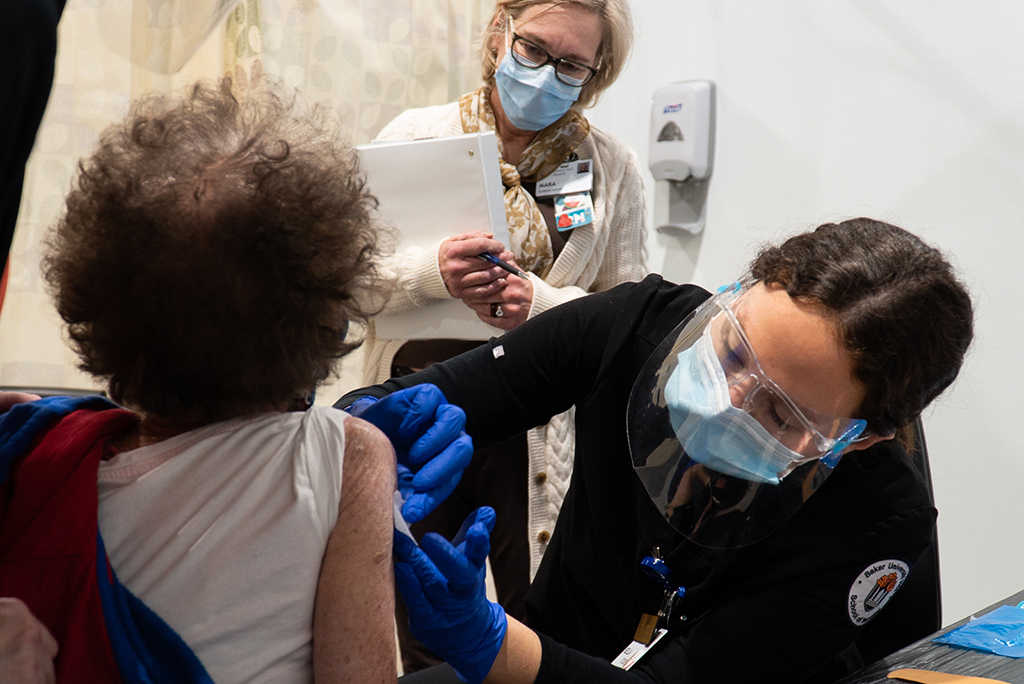 Nursing student giving a woman a COVID vaccine at a clinic while an instructor looks on