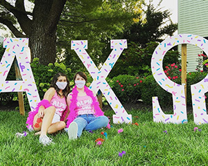 Two women sitting in front of large alpha chi omega letters