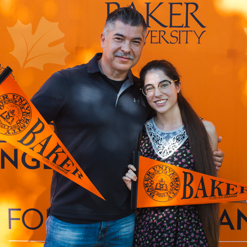 Father and daughter holding Baker pennants in front of a Baker University backdrop