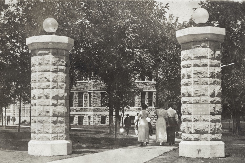 female students in long white dresses walking on Baker campus in the 1900s.